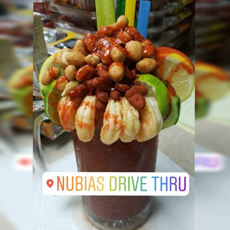 A michelada drink overflowing with shrimp, peanuts, and lime slices, with colorful straws.
