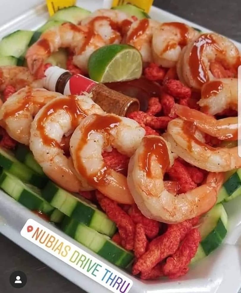 Shrimp cocktail with hot sauce, lime, cucumber slices, and red spicy snacks.