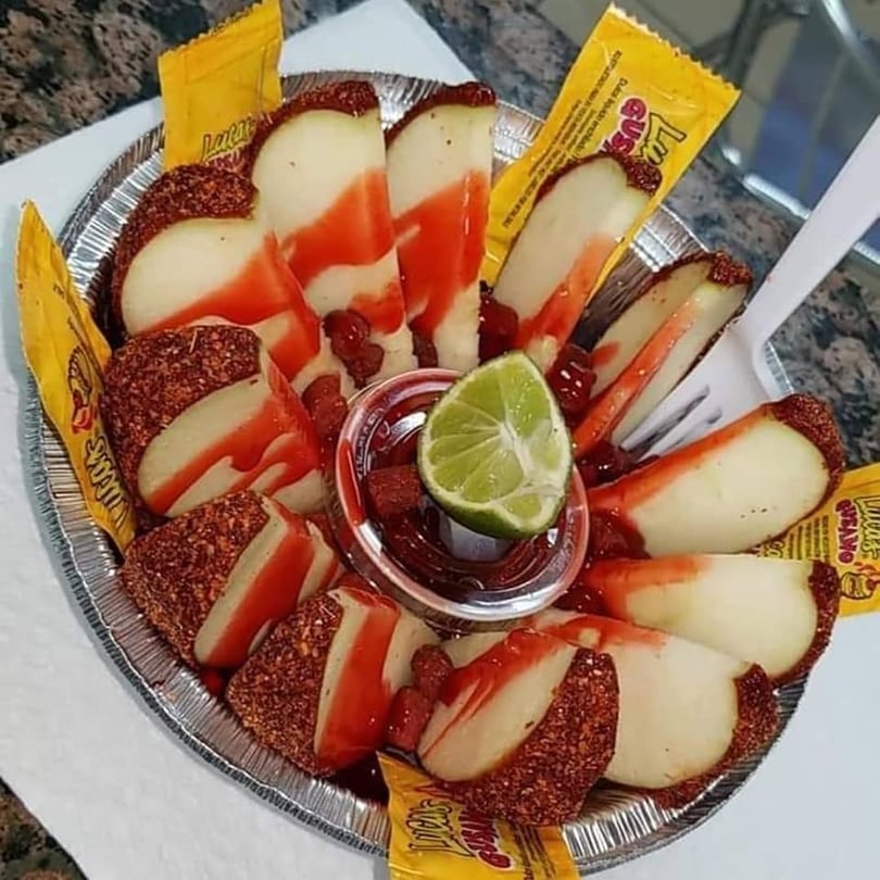 Apple slices with chili powder, red sauce, and a lime wedge in a foil tray.