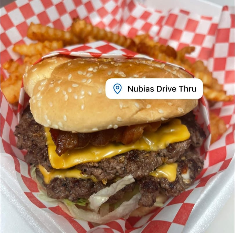 Double cheeseburger with bacon, lettuce, and crinkle-cut fries in a red and white checkered basket.
