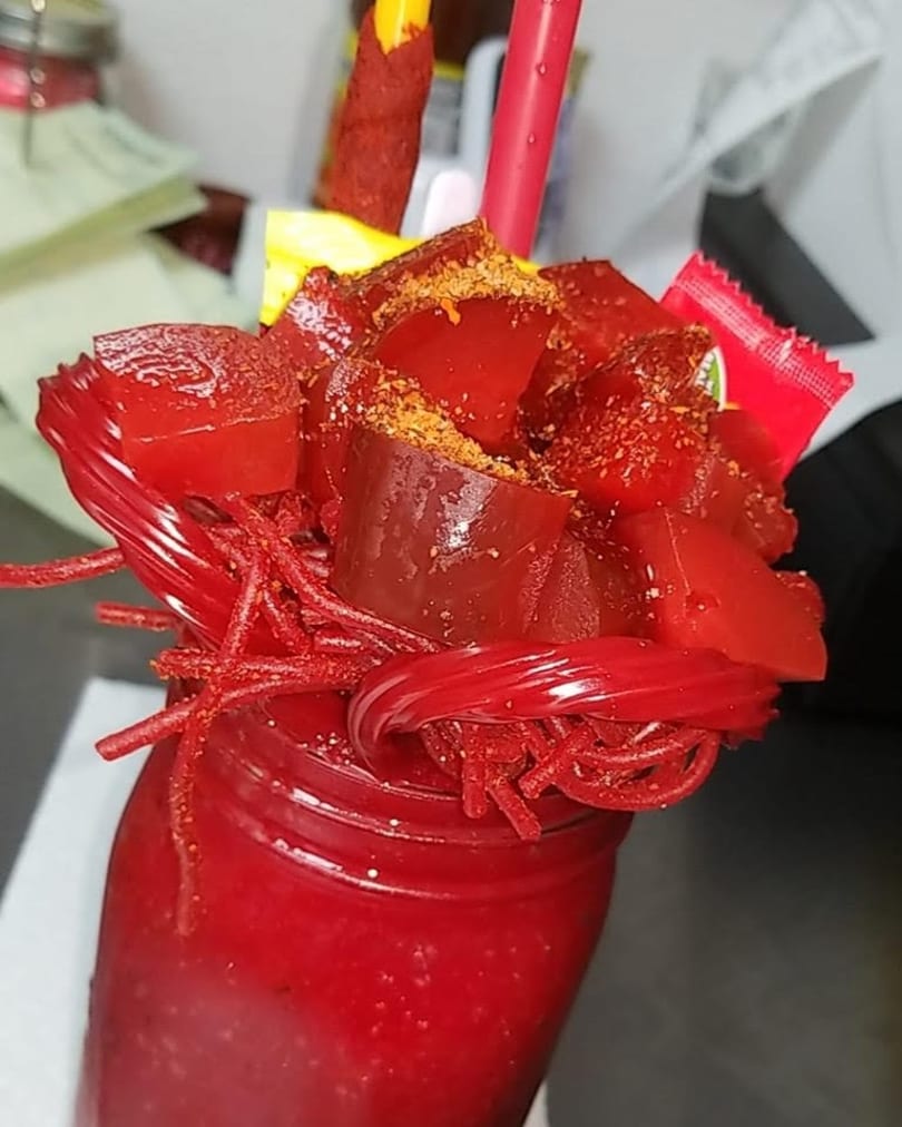 A vibrant red drink in a jar, topped with red gummy candies, licorice, and chili powder.