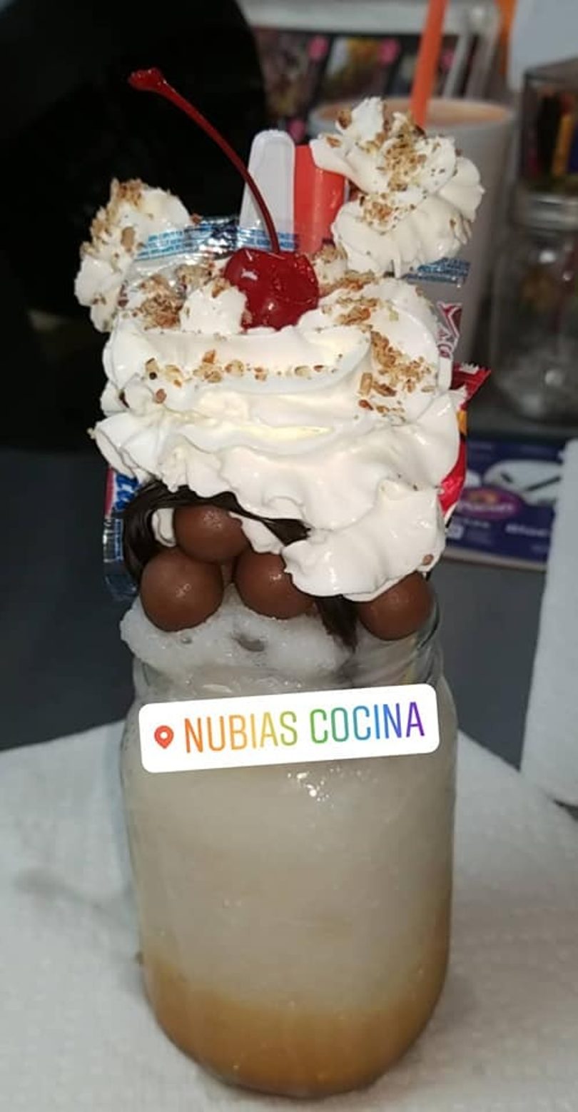 A tall dessert in a glass jar, topped with whipped cream, chocolate balls, and a cherry.